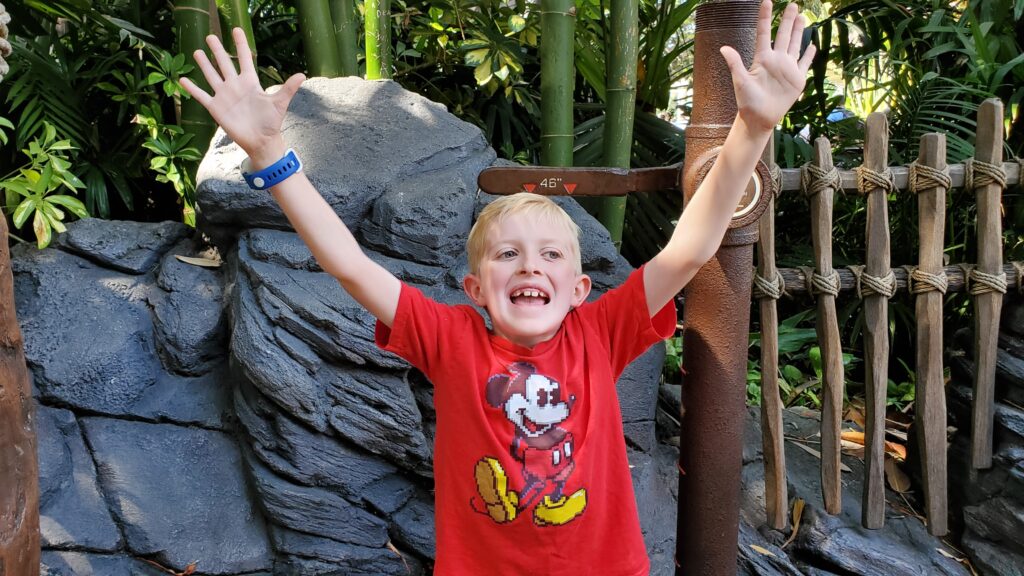 Boy Excited that he hit height requirement, hands up in air celebrating in front of measuring marker at Disneyland.